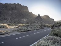 there is a sun setting in the mountains over a road with cars on it and bushes in the foreground