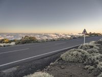 a roadway on a mountain with clouds and trees in the background to a clear, blue sky