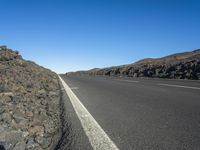 a black road leading away from the desert area with a sky blue background, along with many rocks and boulders