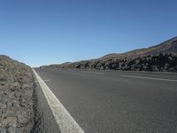 a black road leading away from the desert area with a sky blue background, along with many rocks and boulders