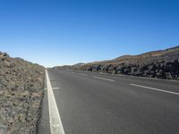 a black road leading away from the desert area with a sky blue background, along with many rocks and boulders