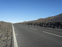 a black road leading away from the desert area with a sky blue background, along with many rocks and boulders