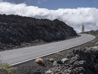 a curved road with the car on it in a barren mountain landscape with grey rock and grass