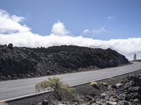 a curved road with the car on it in a barren mountain landscape with grey rock and grass