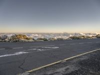 the paved road is next to a large hill above the clouds and on top of a mountain