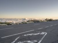 the top of a mountain with the clouds in the sky behind it and the road painted white