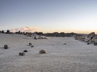 a lone horse is laying in a rocky area near rocks and boulders as the sun goes down