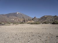 a mountain and some grass and some rocks in the desert near a large hill with a snow capped mountain