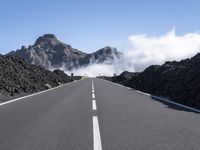 the empty road stretches into the distance at a high altitude with some clouds and steam rising out of the mountains behind