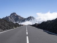 the empty road stretches into the distance at a high altitude with some clouds and steam rising out of the mountains behind