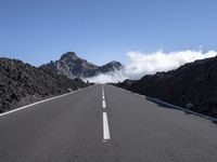 the empty road stretches into the distance at a high altitude with some clouds and steam rising out of the mountains behind