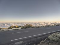 a long paved road passing through the mountains with low clouds below it and mountains above