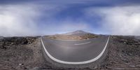 a wide angle lens photo of a curve road surrounded by mountains and clouds at the bottom