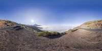 the 360 - view image shows an asphalt road in the distance with two people walking on it and mountains and clouds in the background