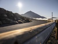 a wooden fence with a mountain in the back ground near a road that runs to some hills