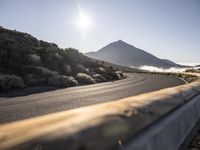 a wooden fence with a mountain in the back ground near a road that runs to some hills