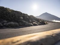 a wooden fence with a mountain in the back ground near a road that runs to some hills