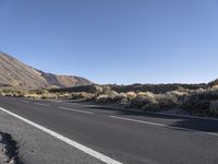 a street with white lines and mountains in the background, in the middle of a desert, on a clear day