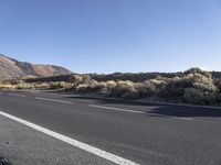 a street with white lines and mountains in the background, in the middle of a desert, on a clear day