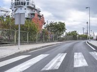 a long road that has been painted a white diagonal crosswalk on it, as a large boat is in the distance