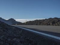 a mountain with rocks and a road next to it on a clear day with a mountain behind