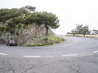 a car driving in front of a rock wall on a road way with trees and rocks