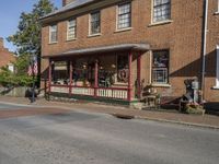 a store with a bench on the porch of it, at the corner of the street and across from a building