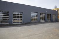 a view of some fire station doors on a grey building in the country side and a road to the right