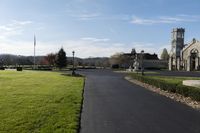 the driveway has gravel and grass surrounding it and a large stone church building with a steeple on top