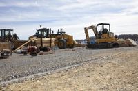 two yellow diggers and a bulldozer sit side by side, beside some gravel