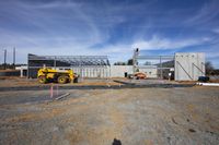 construction equipment on the ground in front of a construction site, including a concrete wall and building and a construction work area