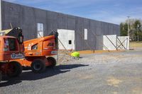 a construction site with two orange vehicles and construction men, working on the wall and placing cement pieces