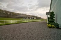 a beautiful house in the countryside during the day with fog in the air, a driveway leading to a barn with a white fence