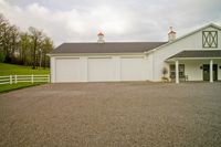 a building with several windows has a white fence and two doors next to it are a horse barn
