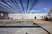 the view of an unfinished warehouse, with lots of equipment in front of it and a worker walking away