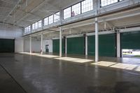 a view of a empty warehouse with green doors and exposed ceilings is open to let the sun in