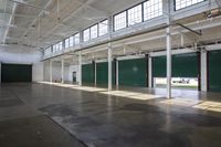 a view of a empty warehouse with green doors and exposed ceilings is open to let the sun in