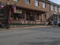 the street is in front of an old house with american flags on it and a trashcan next to the sidewalk