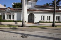 a white house with a red tiled roof and palm trees next to the road in front of it