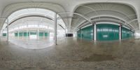 a fish eye lens of the interior of a large warehouse building with green doors and exposed walls