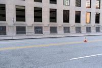 two orange cones are on the side of a city street while a man is riding a bicycle