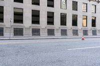 two orange cones are on the side of a city street while a man is riding a bicycle