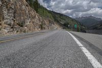 the empty highway winds away from an area that is surrounded by mountain and rocks, with mountains in the distance