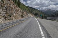 the empty highway winds away from an area that is surrounded by mountain and rocks, with mountains in the distance