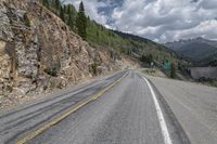 the empty highway winds away from an area that is surrounded by mountain and rocks, with mountains in the distance