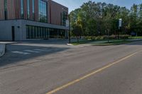 a empty street in front of the building, with trees outside and a person on a motor scooter on the right