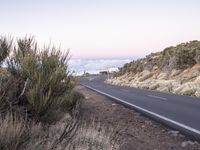 an empty winding road on a mountain with the sun set above the mountains in the background