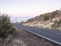 an empty winding road on a mountain with the sun set above the mountains in the background