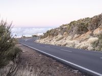 an empty winding road on a mountain with the sun set above the mountains in the background