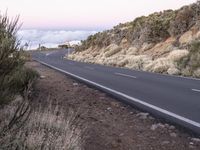 an empty winding road on a mountain with the sun set above the mountains in the background